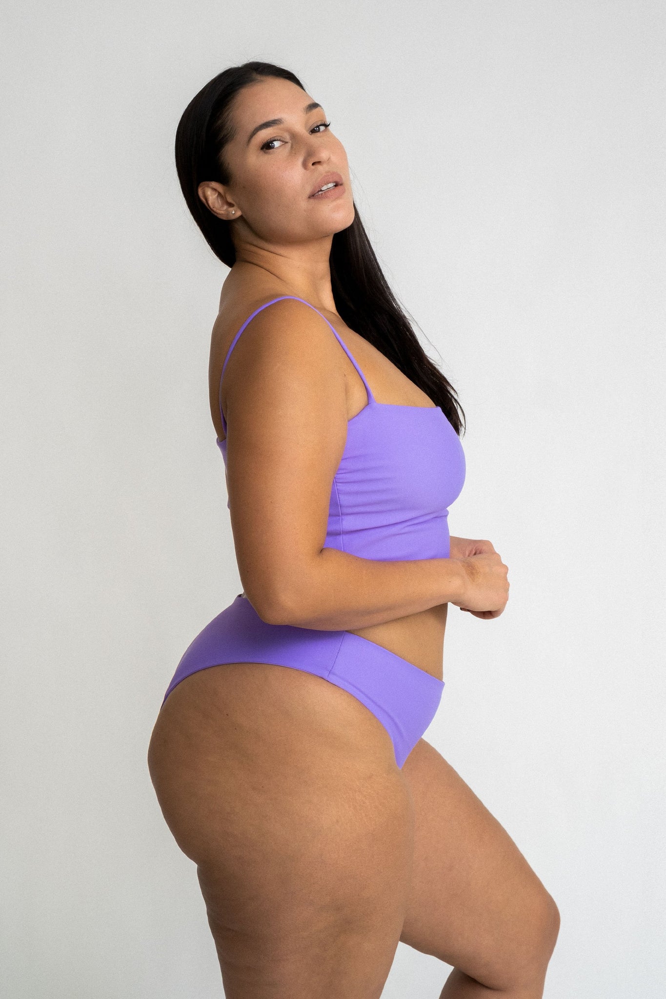 The side profile of a woman wearing bright lavender high cut bikini bottoms and a matching bright lavender tankini top.
