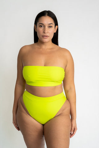 A woman standing with her arms by her side wearing bright neon green high waisted bikini bottoms with a matching bright neon green strapless bandeau bikini top.