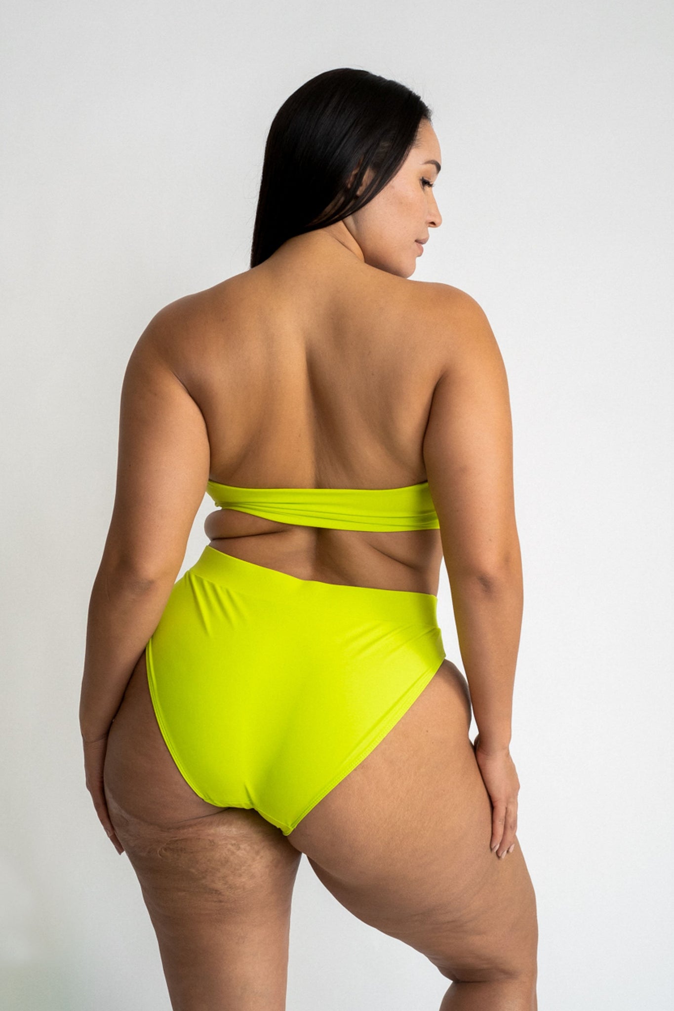 The back of a woman wearing bright neon green high waisted bikini bottoms with a matching bright neon green strapless bandeau bikini top.