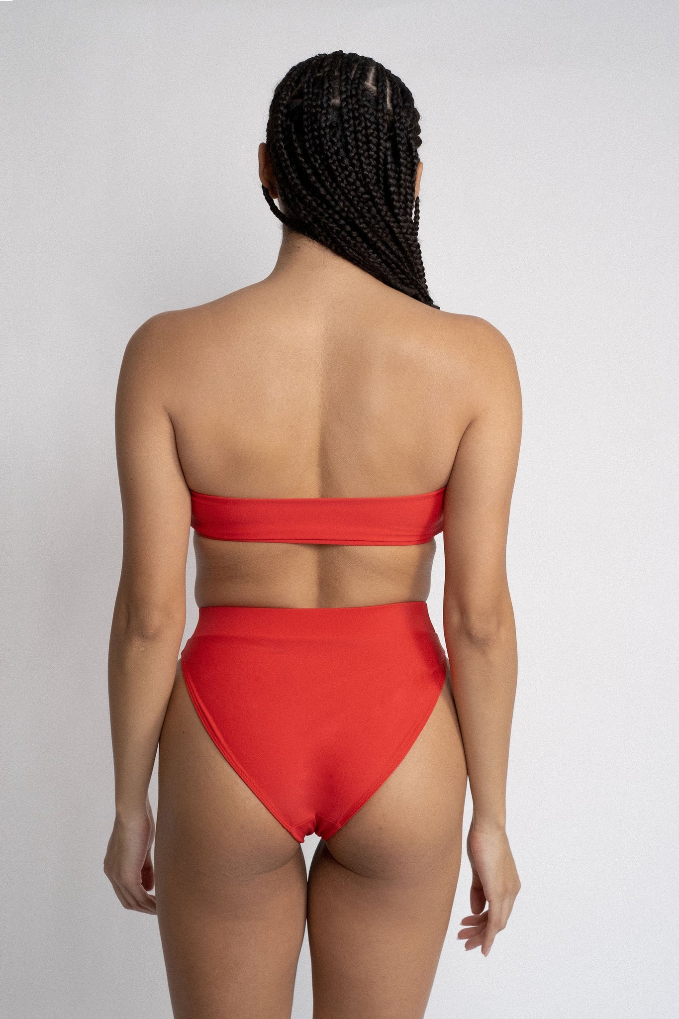 The back of a woman with her arms by her side wearing bright red high waisted bikini bottoms with a matching bright red strapless bandeau bikini top.