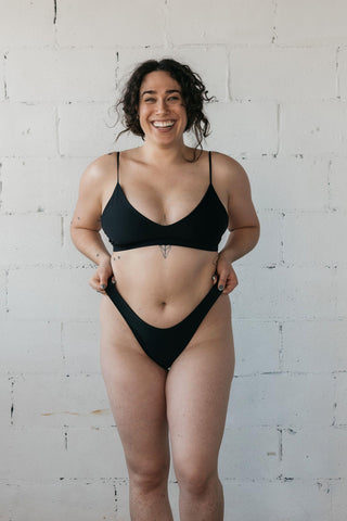 Woman smiling wearing minimal coverage black bikini holding bikini bottoms