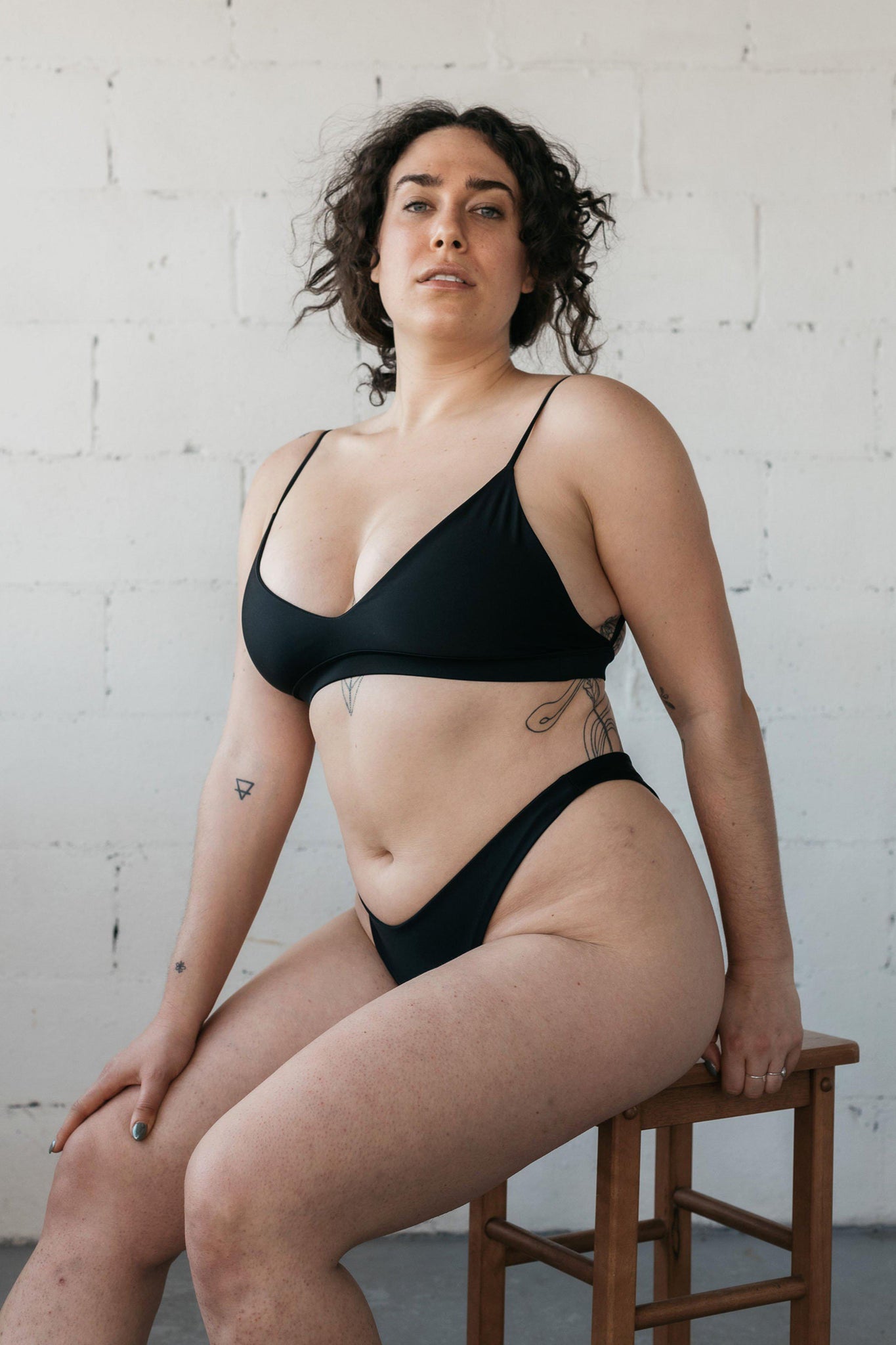 Woman sitting on a stool wearing a black bikini with high cut bottoms