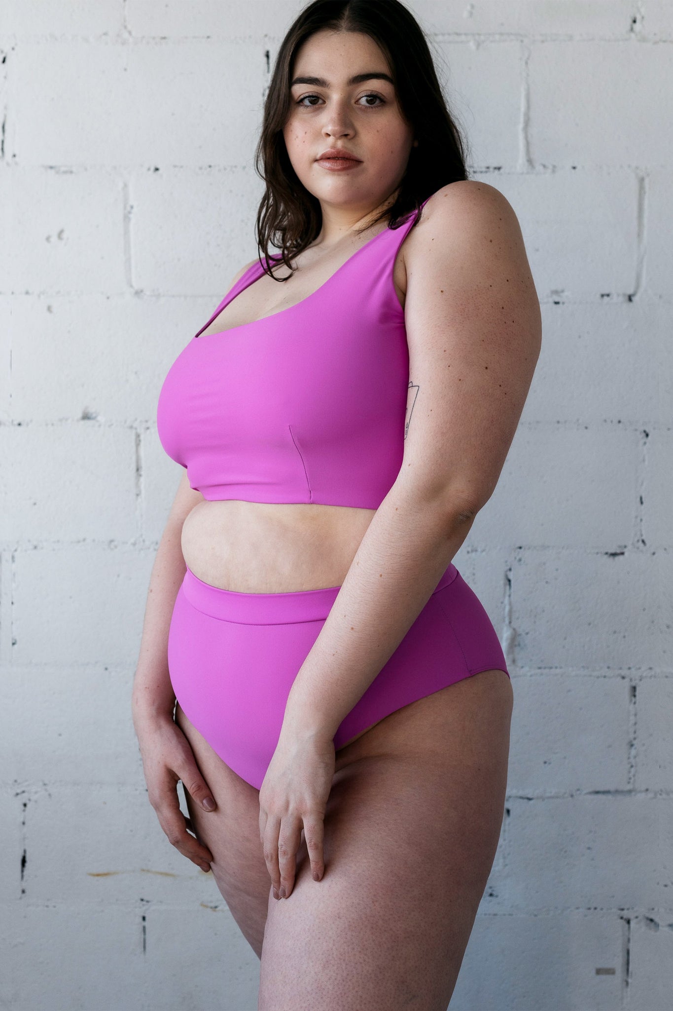 A woman standing in a bright purple high waisted bikini bottoms with a full coverage bikini top.