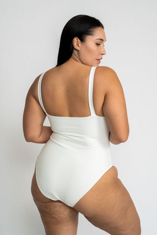The back of a woman looking over her shoulder wearing a white one piece swimsuit with minimal coverage.