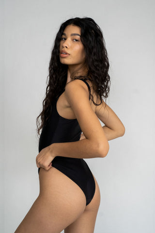 The back of a woman looking over her shoulder wearing a black one piece swimsuit with a straight neckline.